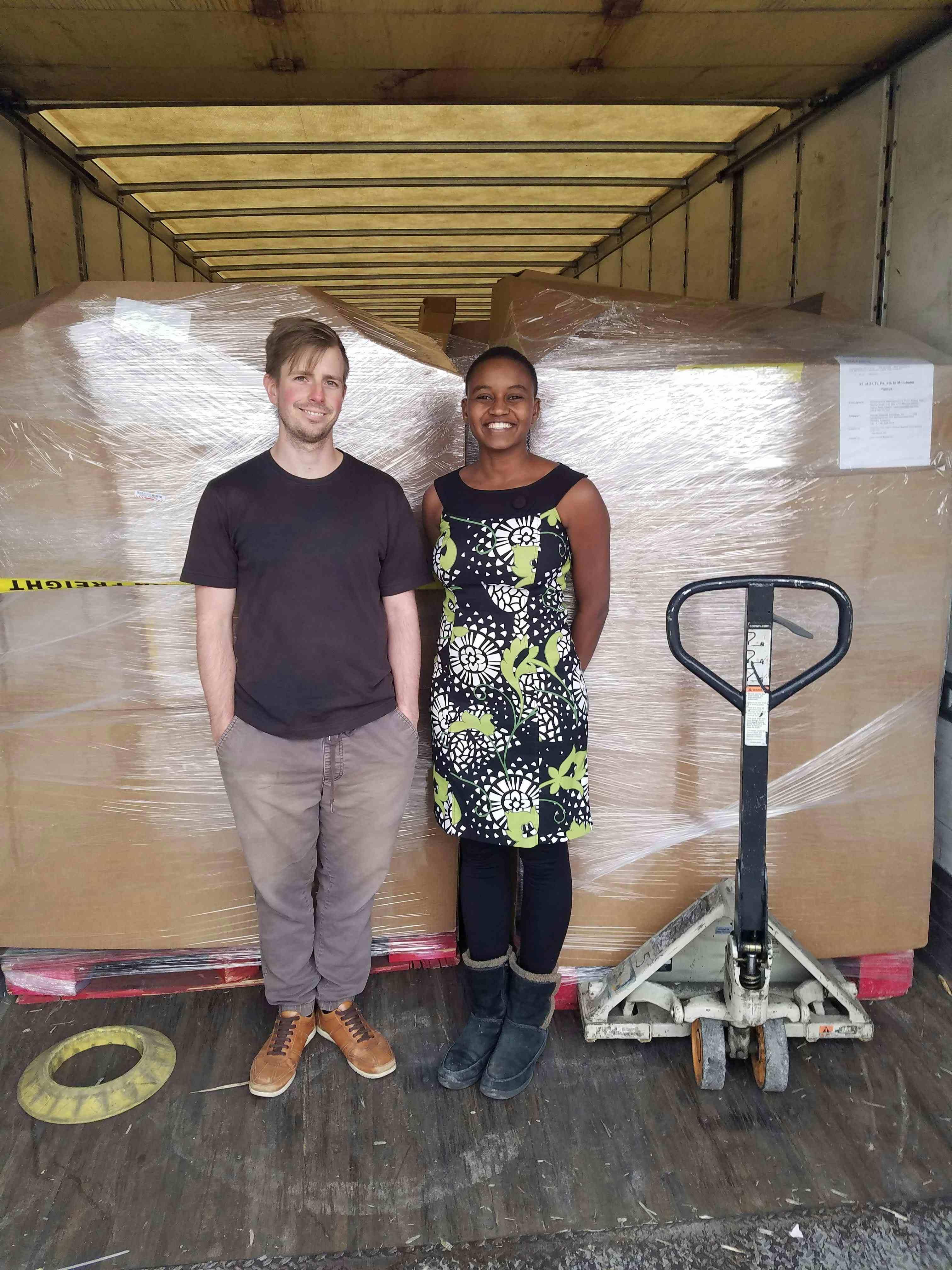 Nelly Cheboi and Tyler Cinnamon standing before a pallet of computer