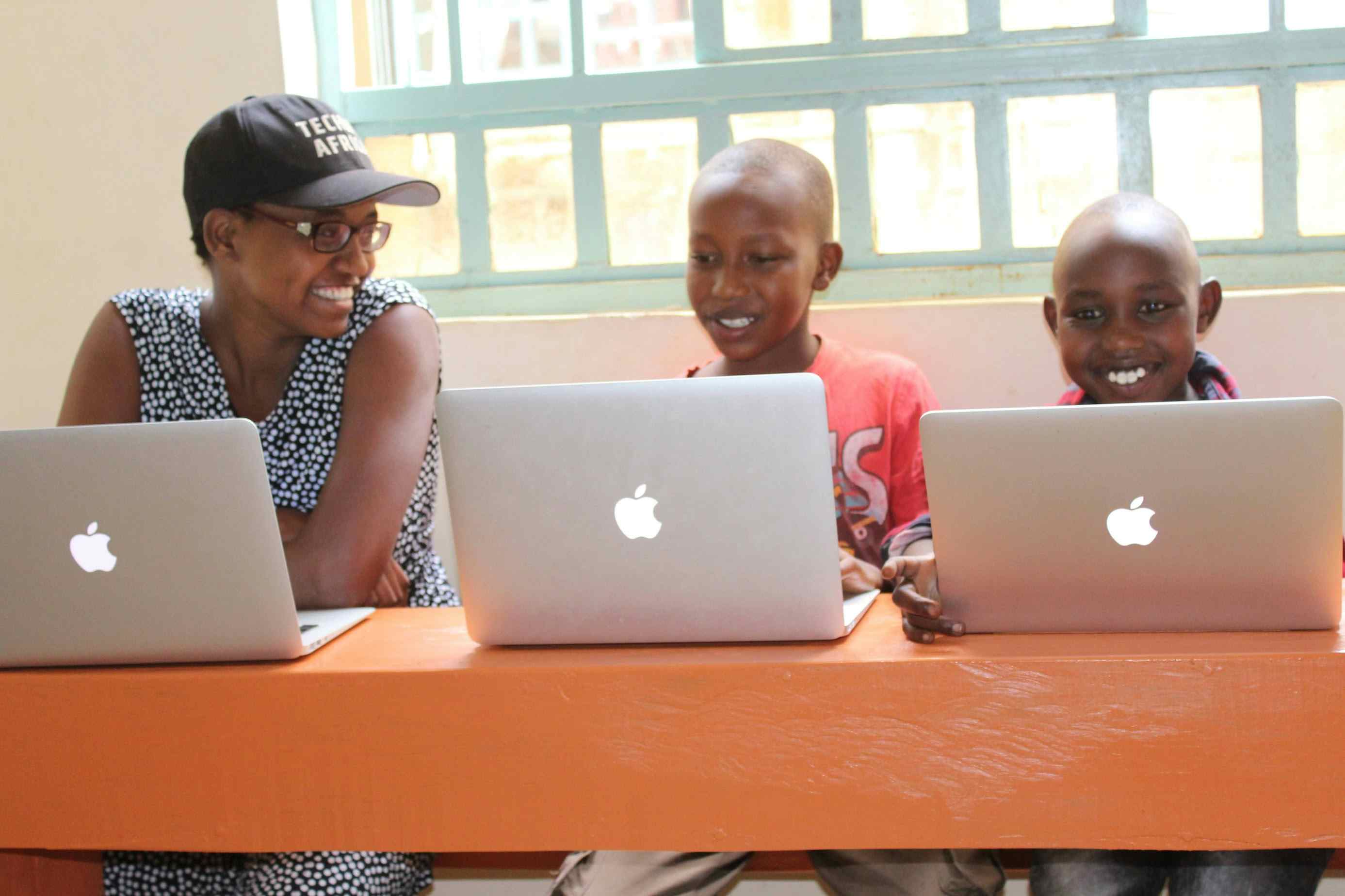 Nelly Cheboi smiling with kids using donated macbook computers